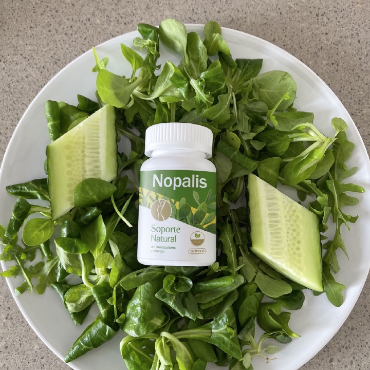 Frasco de Nopalis sobre un plato con hojas verdes y pepino